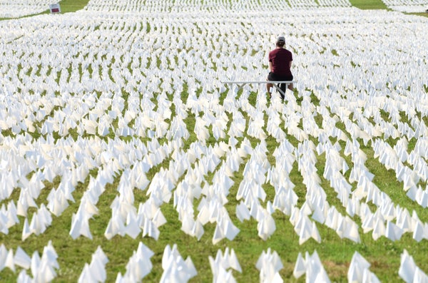 A person sitting on a bench surrounded by small white flags.