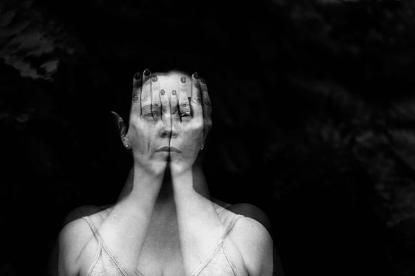 A double exposure image of a woman's face on a woman's hands covering her face.