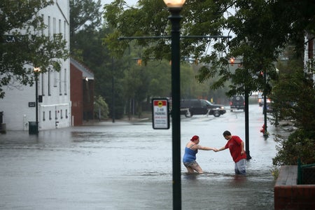 Two people navigate flooded streets in a neighborhood.