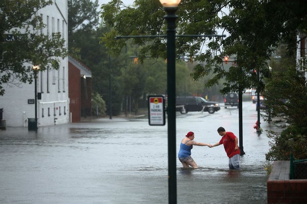 Two people navigate flooded streets in a neighborhood.