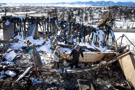 People wander through the charred remains of a burned home