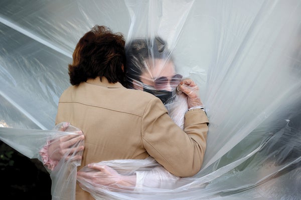 Grandmother and granddaughter hug through a plastic drop cloth.