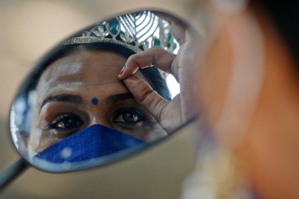 A person with a tiara and sculped eyebrows is partially visible in a mirror.