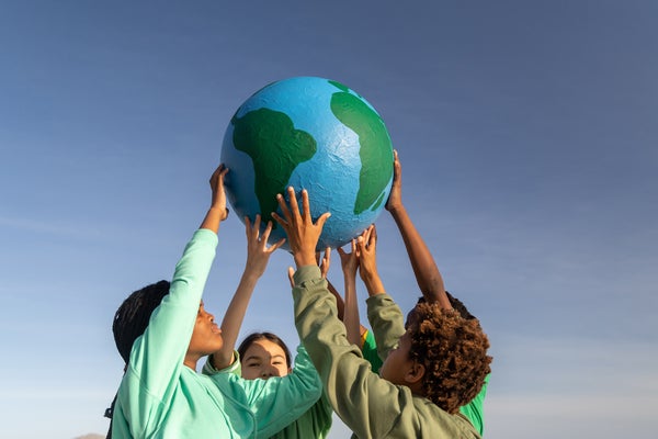 Group of children working together to hold a model of Earth above their heads, shown against a blue sky.