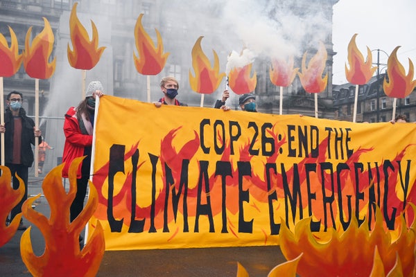 Activists surrounded by smoke hold up flame-decorated "Climate Emergency" signs.