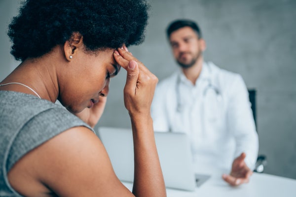 African-american woman sitting opposite the doctor in his office and holding her head with hands.