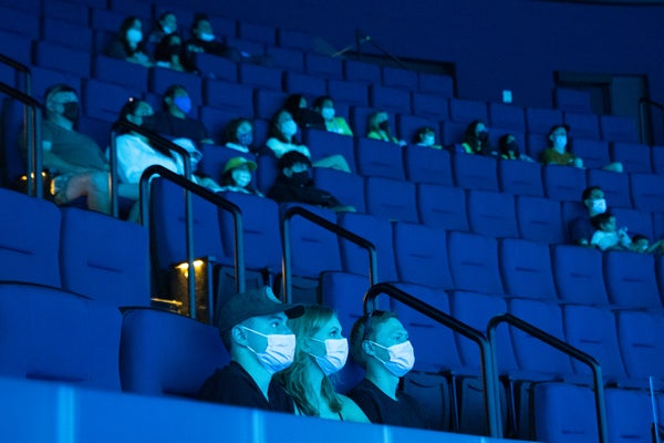 Visitors wearing masks watch a film inside a theater at the Aquarium of the Pacific in Long Beach, Calif.