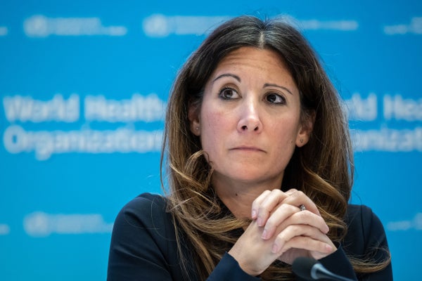 Maria Van Kerkhove is pictured sitting at a table during a press conference in front of a blue backdrop with the World Health Orginzation's logo