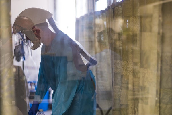 A Covid nurse on the unit, seen through a pane of glass.