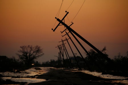 Utility poles bent over road with car headiights seen in distance.