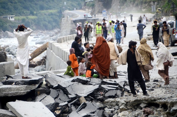 People gather on top of stones near a destroyed bridge