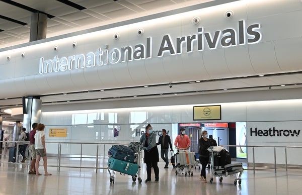 Passengers walk through the arrivals hall after landing at Terminal Two of London Heathrow Airport in front of INTERNATIONAL ARRIVALS sign.