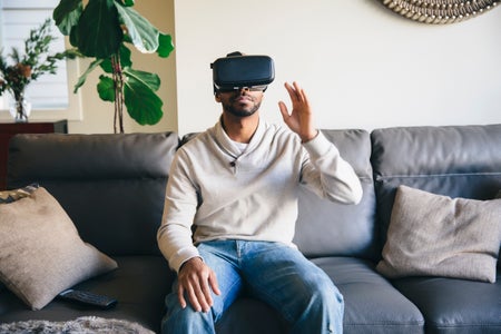 A man site on a couch wearing a virtual reality headset.