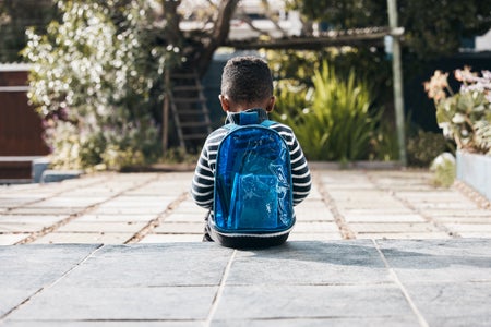 Little boy sitting outside with his backpack