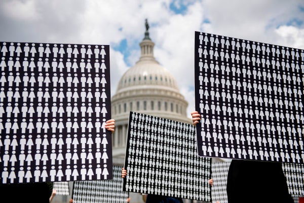 With the U.S. Capitol dome in the background, hands gripping black posters covered with tiny white cartoon figures of men and women.