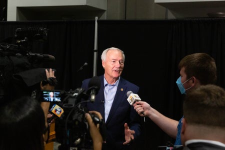 A tieless governor of Arkansas speaks to the press about his campaign to get Arkansans vaccinated.