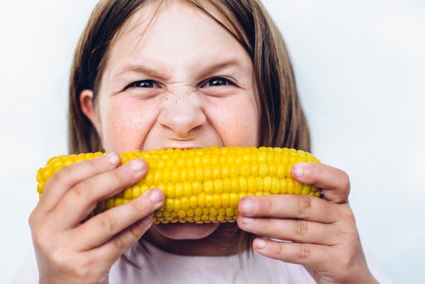 A preteen girl bites into an ear of sweet corn