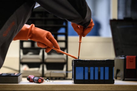 Close up of hands of a mechanic with orange gloves working on a battery module of an electric car.