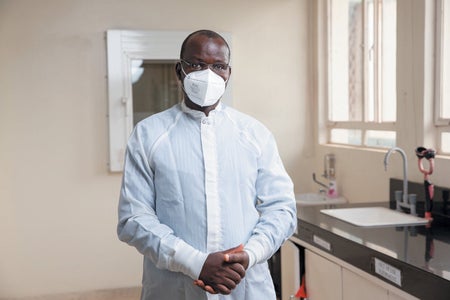Willy Ssengooba wearing white medical robe and face mask.