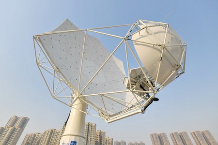 A radio dish stands in front of a group of buildings.