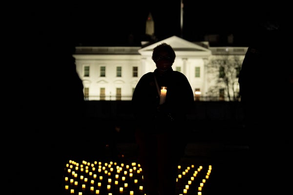 A silhouette of a person holding a candle at a vigil with the White House in the background.