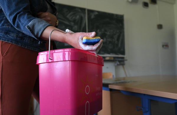 A person holding a pink bucket cleans and disinfects a classroom.