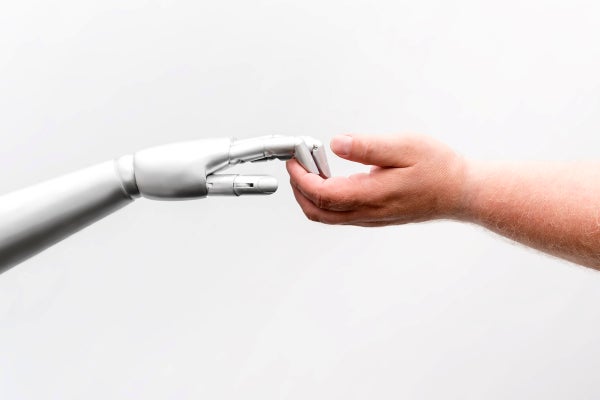 A human hand lightly grasps the hand of a robot.