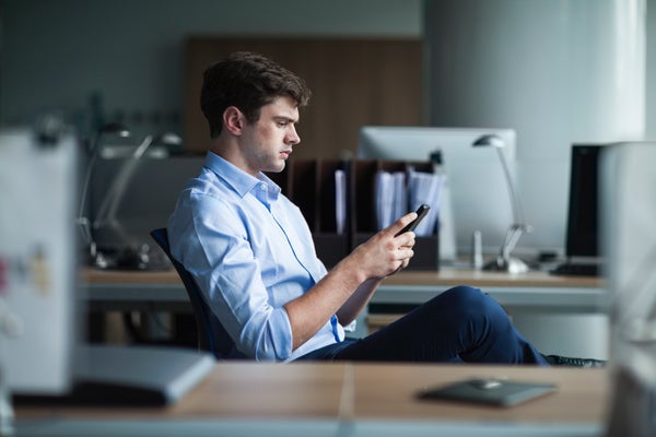 A man sits at a desk looking intently at his smartphone.