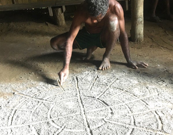 A Vanuatuan sand drawing artist traces a circular grid on a sandy floor