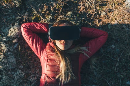 Young woman with VR goggles lying on ground in nature