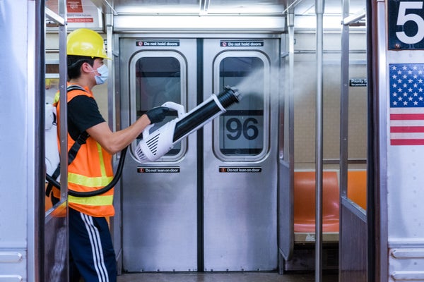 A person wearing a safety vest and a mask sprays disinfectant inside a subway car