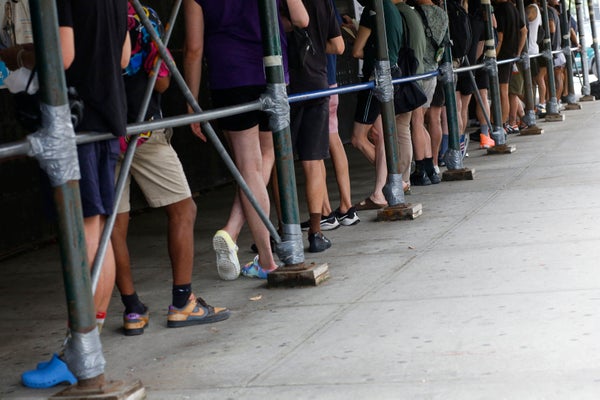 People standing under scaffolding on sidewalk