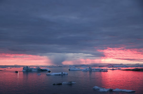 Floating icebergs are shown against a colorful sunset in Greenland.