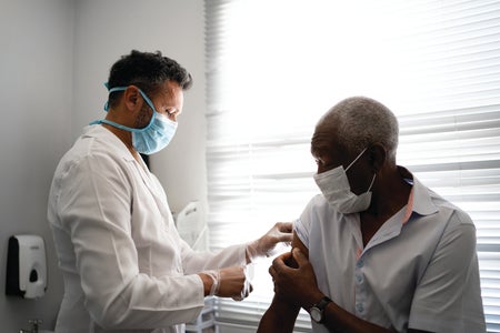 Doctor administering vaccine to an elderly black man.