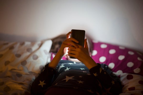 A child lies on a bed, their face obscured by a smartphone.