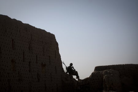 A armed man sits silhouetted against the sky.