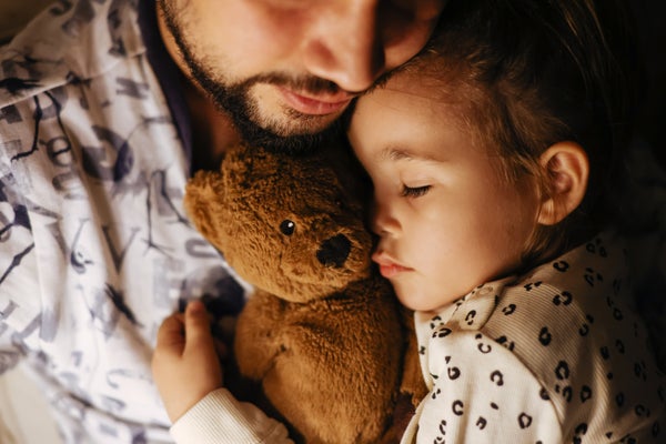 Father holding sleeping toddler daughter and teddy bear