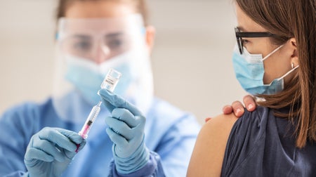 Young female teenager is getting her vaccination dose against coronavirus from a medical worker.