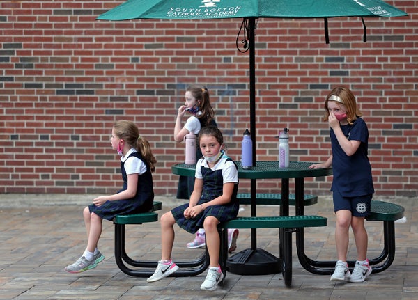Schoolgirls sit outside at a table without face masks.