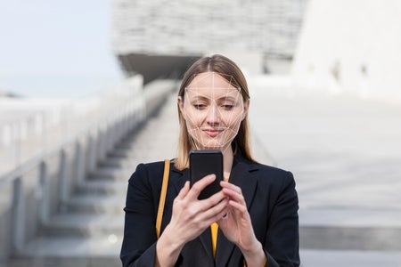 Woman unlocking mobile phone with face recognition technology while standing outdoors