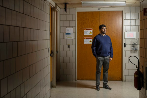 Ranga Dias with a blue sweater in front of a brown wooden door in the hallways of Rochester University