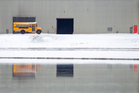 Yellow school bus parked on snow, with reflection in water