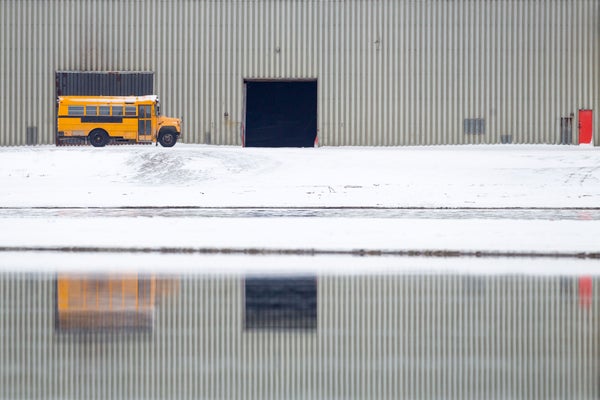 Yellow school bus parked on snow, with reflection in water