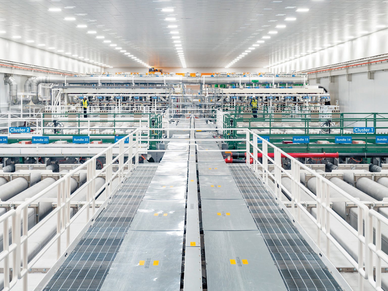  A very long industrial interior space with a long metal walkway above long white tubes carrying the laser beams.