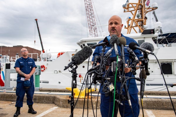 A U.S. Coast Guard captain speaks to the press in front of a Coast Guard boat.