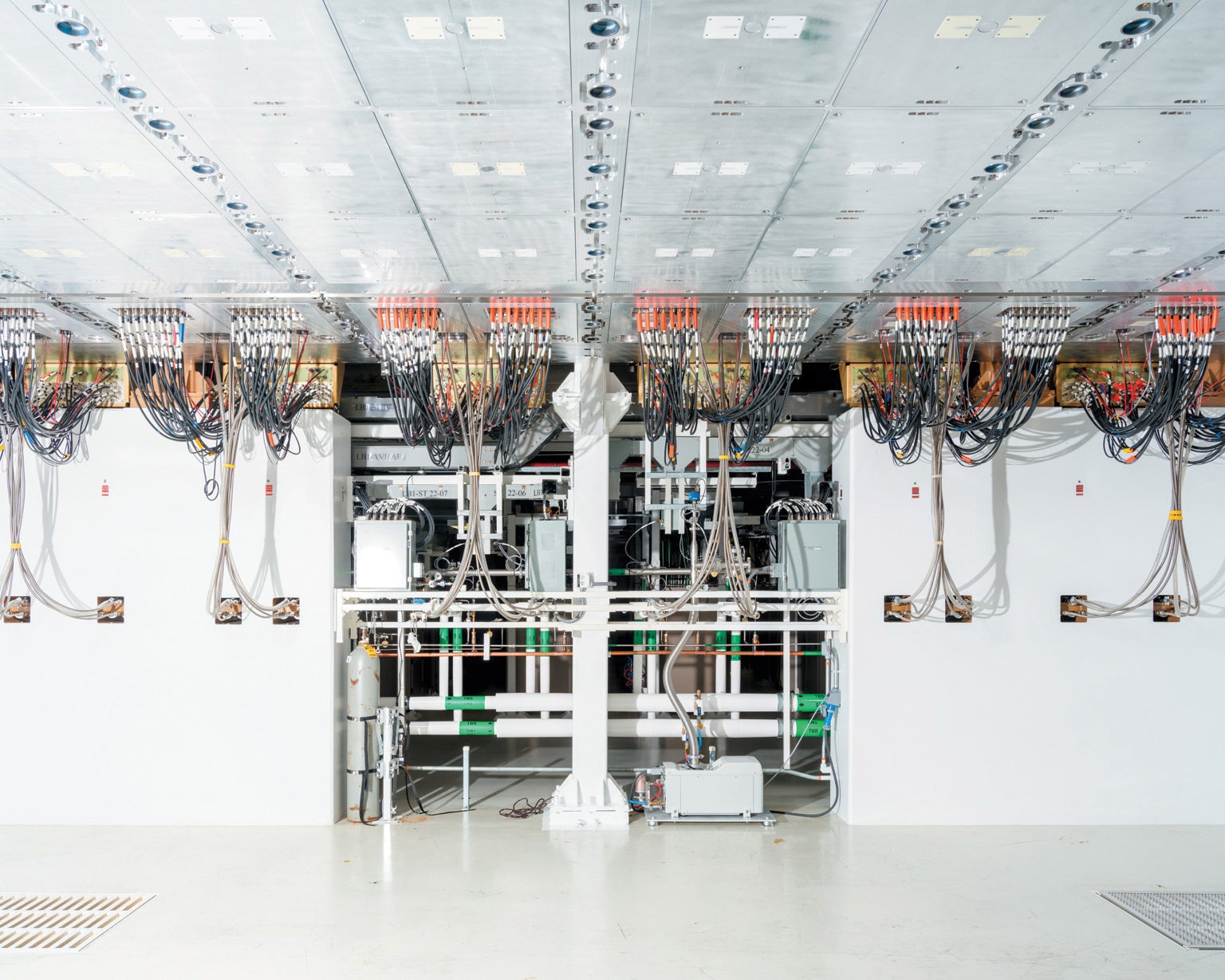  A mostly white shiny space with vertical and horizontal tubes and hanging wires crisscrossing near the ceiling.