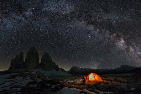 Lonely Camper in front of illuminated tent in Dolomites under Milky Way at Tre Cime of the Dolomites (Drei Zinnen)