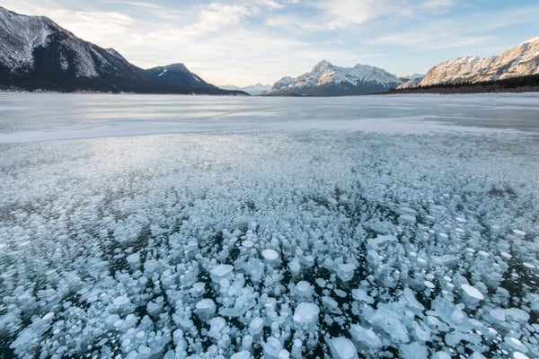 View of frozen lake surface with trapped bubbles and distant mountains.