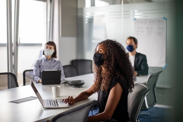 Two women and one man sit in a conference room wearing masks.