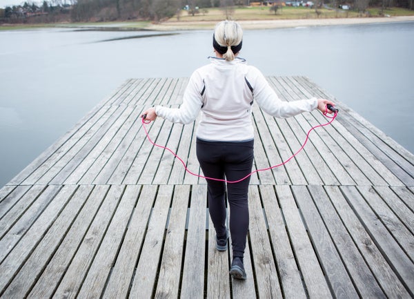 Backview of a mature woman jumping rope on a wooden deck.